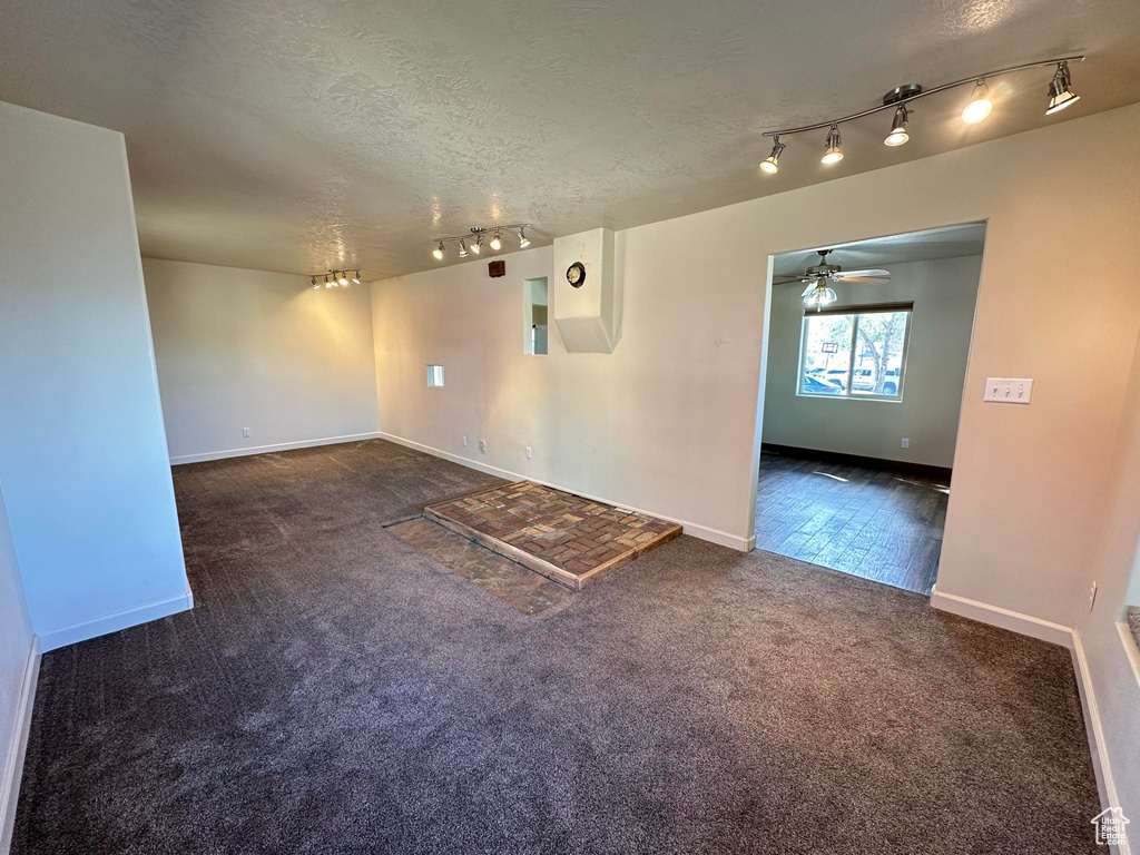 Spare room with ceiling fan, dark carpet, track lighting, and a textured ceiling