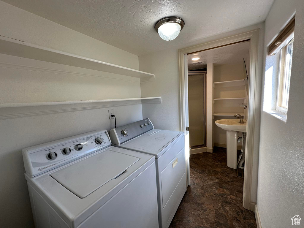 Clothes washing area with a textured ceiling, dark tile flooring, washing machine and dryer, and sink