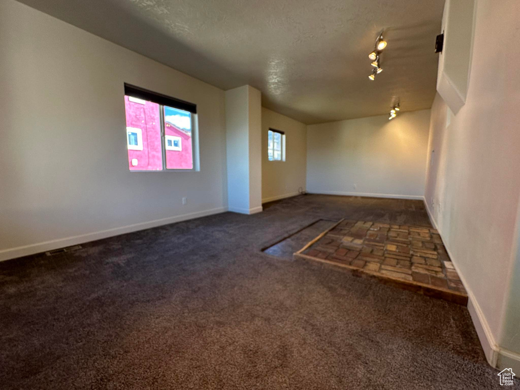 Empty room featuring rail lighting, dark colored carpet, and a textured ceiling