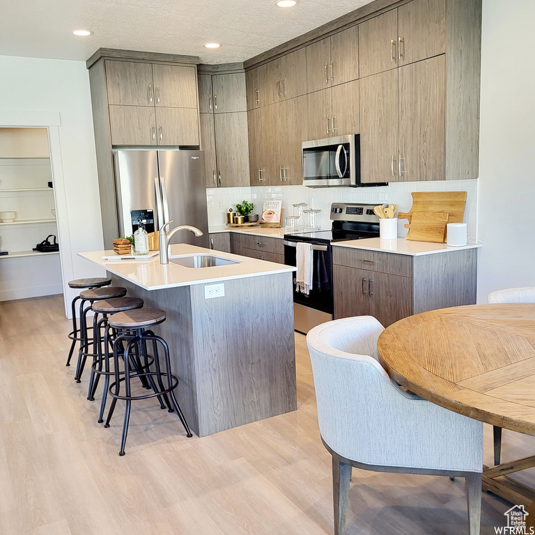 Kitchen with a center island with sink, light hardwood / wood-style floors, stainless steel appliances, and a breakfast bar area