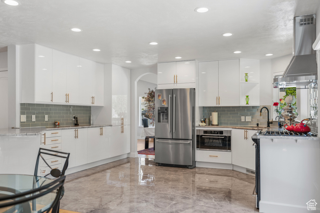 Kitchen featuring backsplash, stainless steel appliances, wall chimney exhaust hood, and white cabinetry