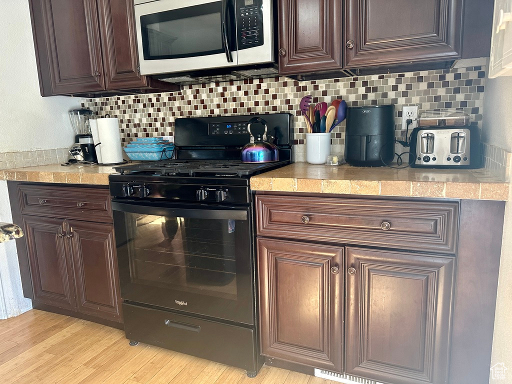 Kitchen with tasteful backsplash, light hardwood / wood-style flooring, black range with gas stovetop, and dark brown cabinetry