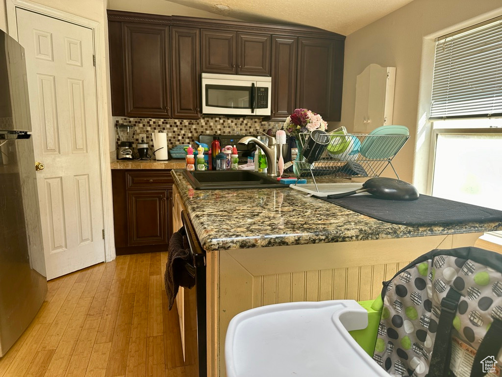 Kitchen with light wood-type flooring, stainless steel appliances, sink, tasteful backsplash, and dark brown cabinetry