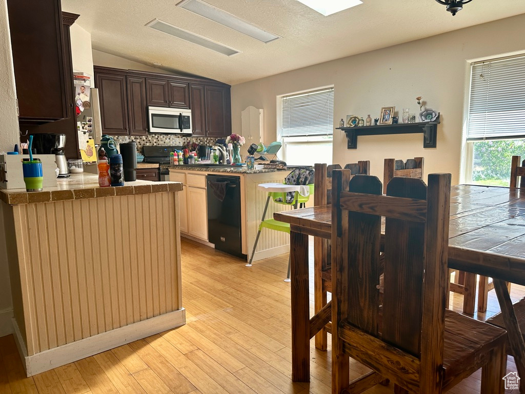Kitchen with backsplash, vaulted ceiling, light hardwood / wood-style floors, dishwasher, and dark brown cabinetry