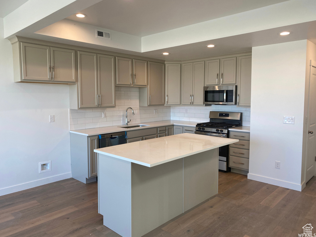 Kitchen featuring appliances with stainless steel finishes, a kitchen island, sink, tasteful backsplash, and dark hardwood / wood-style flooring