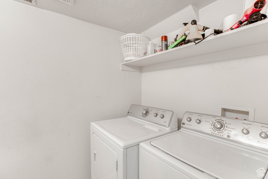 Washroom with a textured ceiling, washer hookup, and washer and clothes dryer