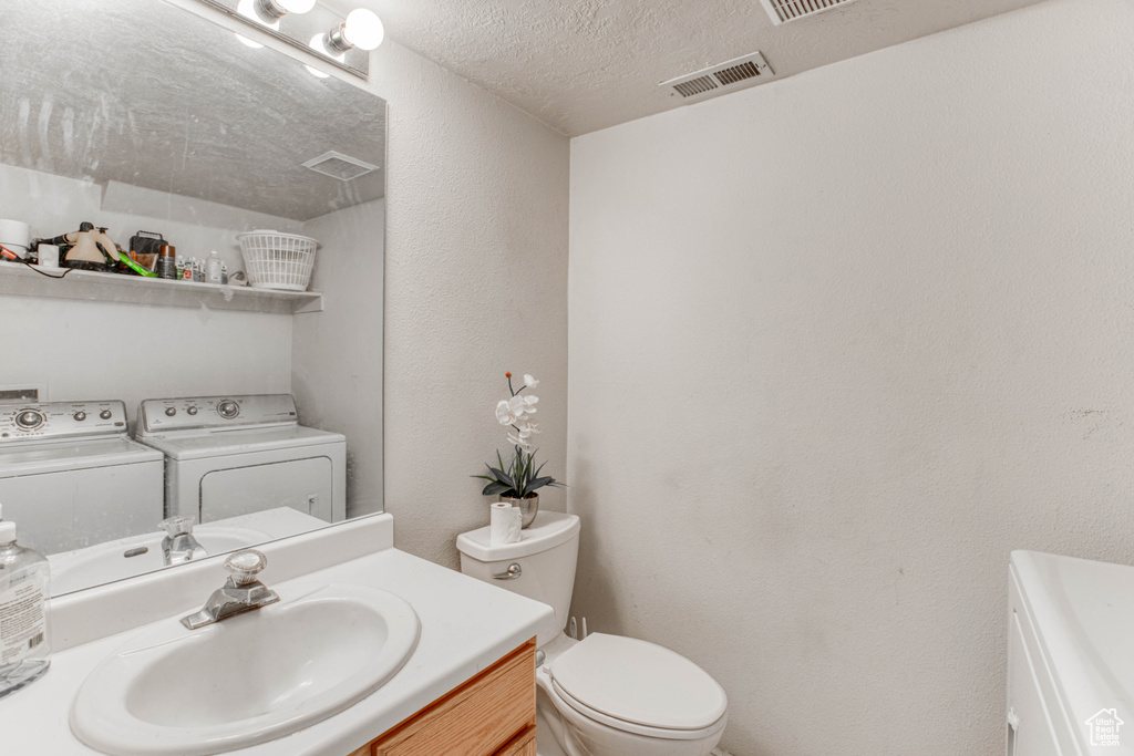 Bathroom with independent washer and dryer, a textured ceiling, toilet, and vanity with extensive cabinet space
