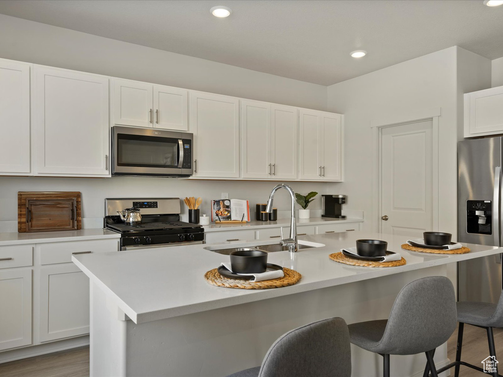 Kitchen featuring hardwood / wood-style flooring, stainless steel appliances, white cabinets, and an island with sink
