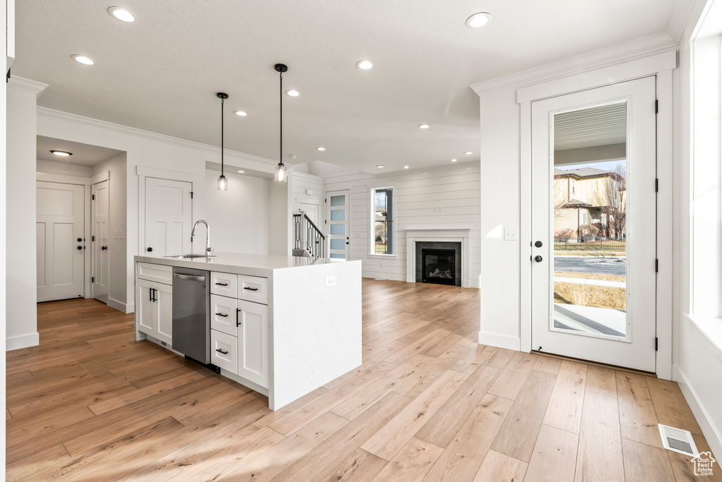 Kitchen with hanging light fixtures, white cabinetry, sink, and light wood-type flooring