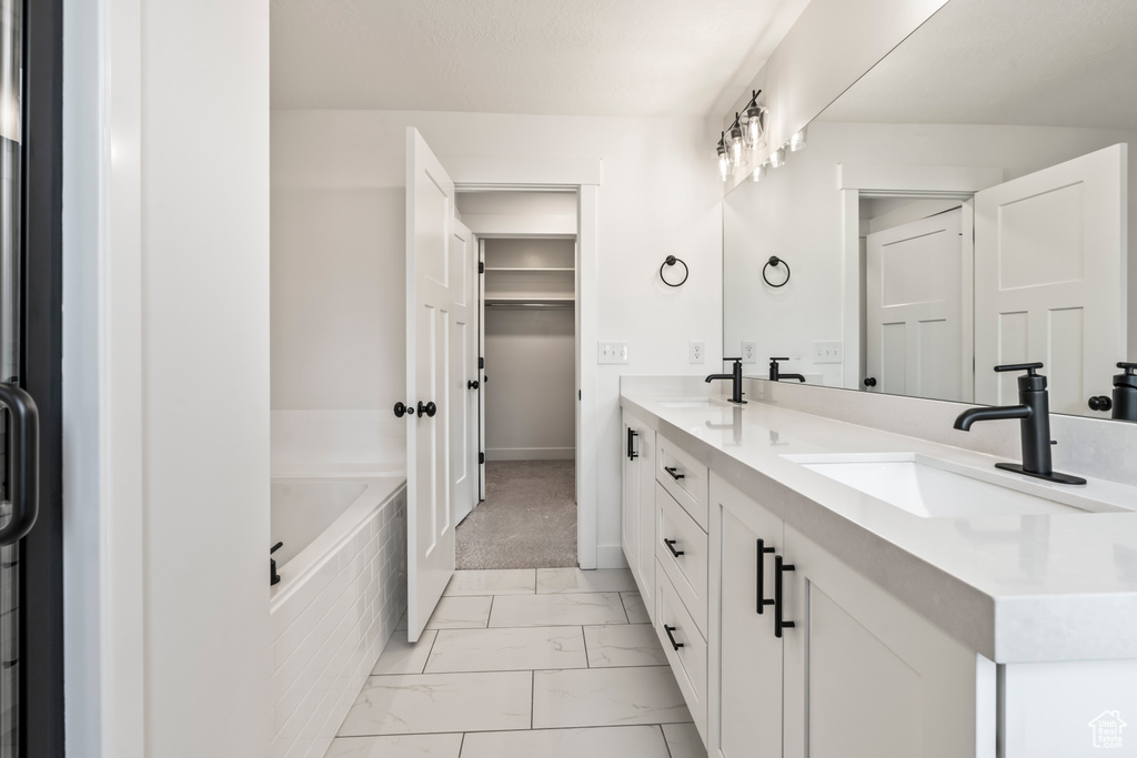Bathroom featuring tile flooring, dual sinks, oversized vanity, and tiled tub