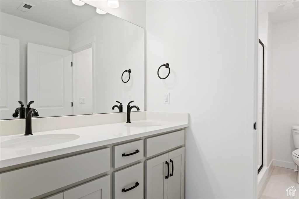 Bathroom featuring oversized vanity, dual sinks, toilet, tile flooring, and a shower with door