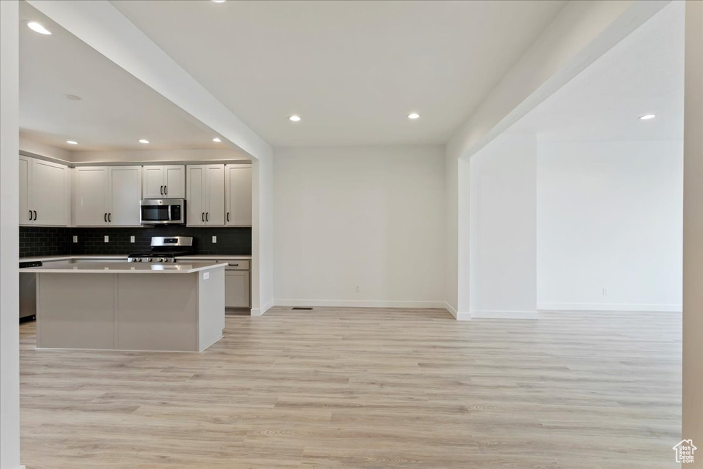 Kitchen featuring tasteful backsplash, range, light hardwood / wood-style floors, and a kitchen island with sink