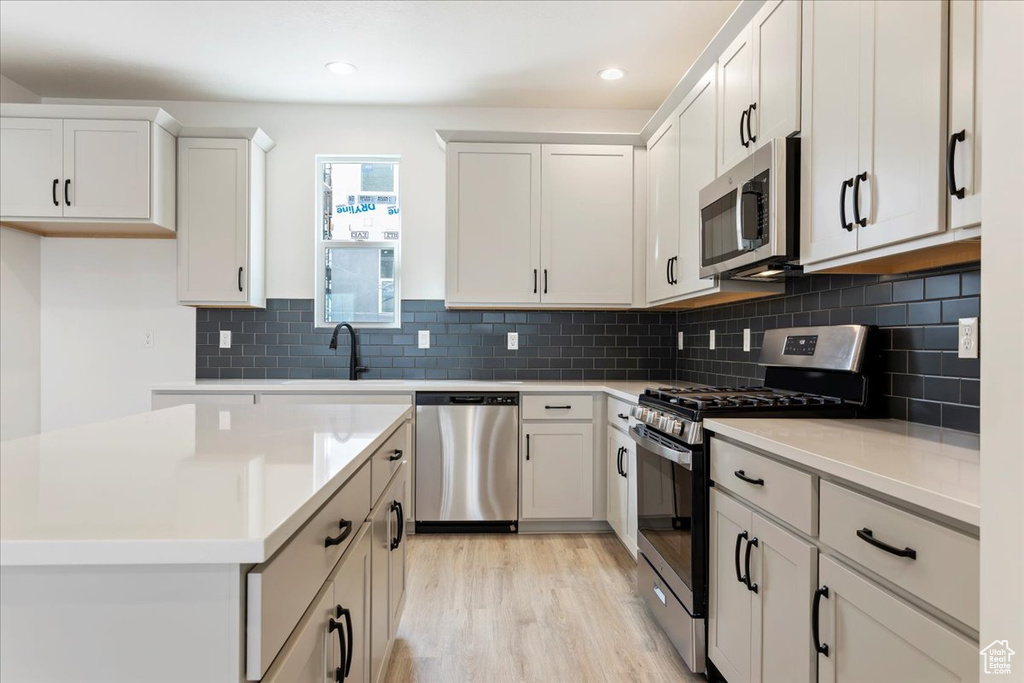 Kitchen with white cabinets, tasteful backsplash, light hardwood / wood-style flooring, and stainless steel appliances