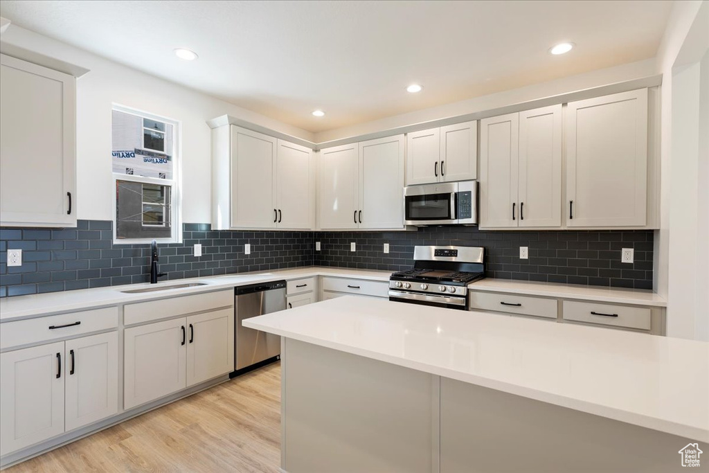 Kitchen featuring light hardwood / wood-style flooring, stainless steel appliances, white cabinets, backsplash, and sink