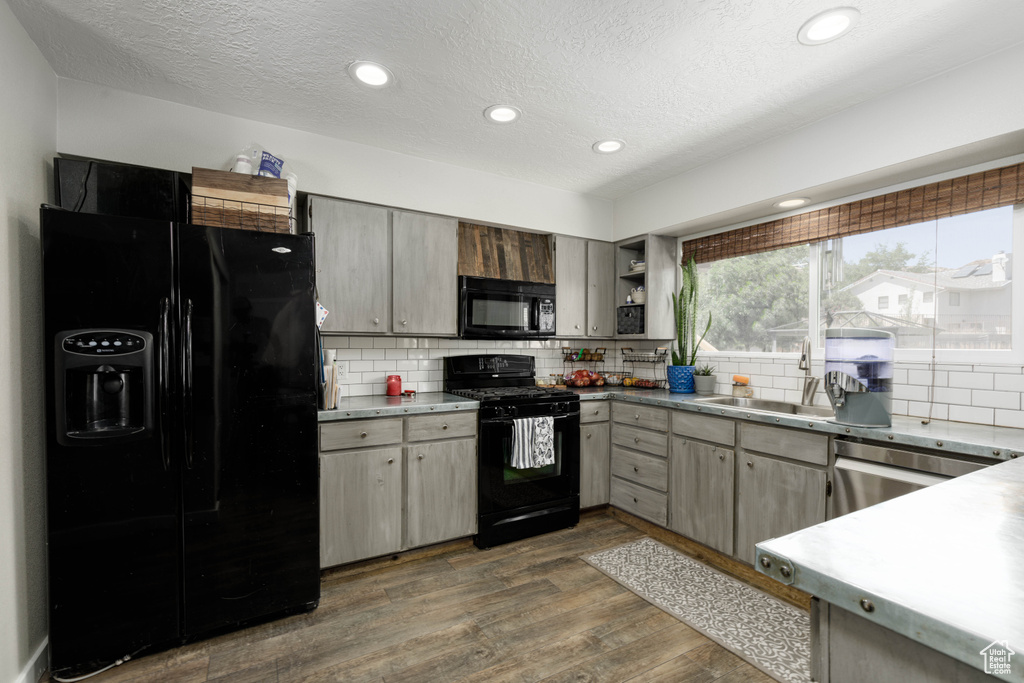 Kitchen with dark hardwood / wood-style flooring, black appliances, backsplash, sink, and a textured ceiling