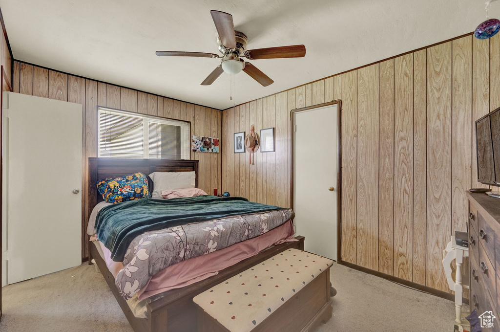 Bedroom featuring light colored carpet, ceiling fan, and wood walls