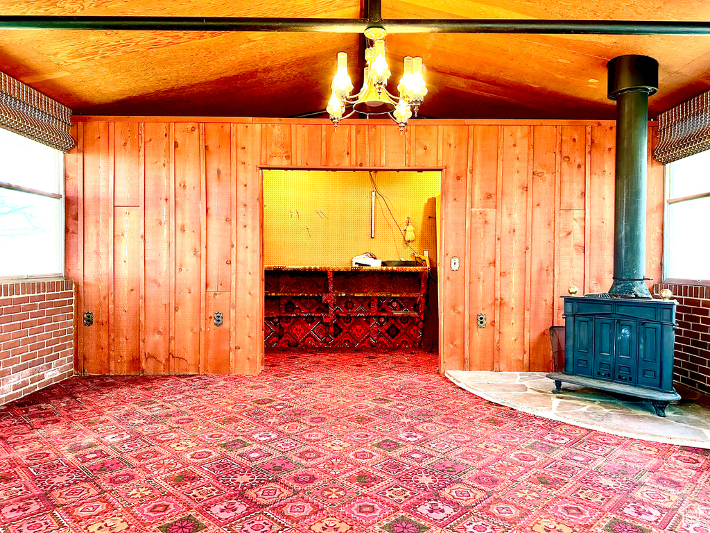 Unfurnished living room featuring vaulted ceiling, wooden ceiling, wood walls, a wood stove, and an inviting chandelier