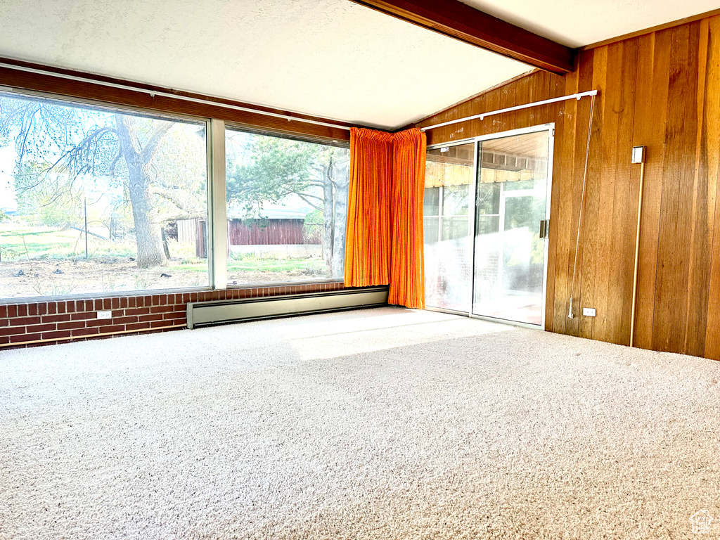 Unfurnished room featuring vaulted ceiling with beams, wood walls, a baseboard heating unit, and carpet floors