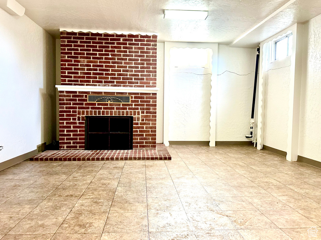 Unfurnished living room featuring tile flooring, a brick fireplace, and a textured ceiling