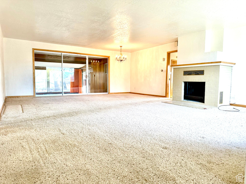 Unfurnished living room with carpet, a notable chandelier, a brick fireplace, and a textured ceiling