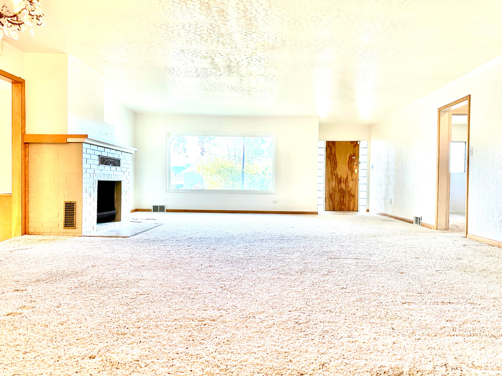 Unfurnished living room featuring carpet, a brick fireplace, and a textured ceiling