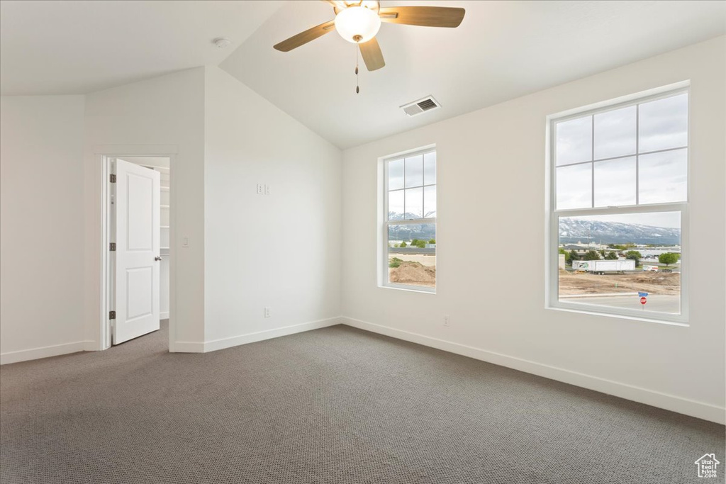 Empty room with ceiling fan, dark colored carpet, and vaulted ceiling