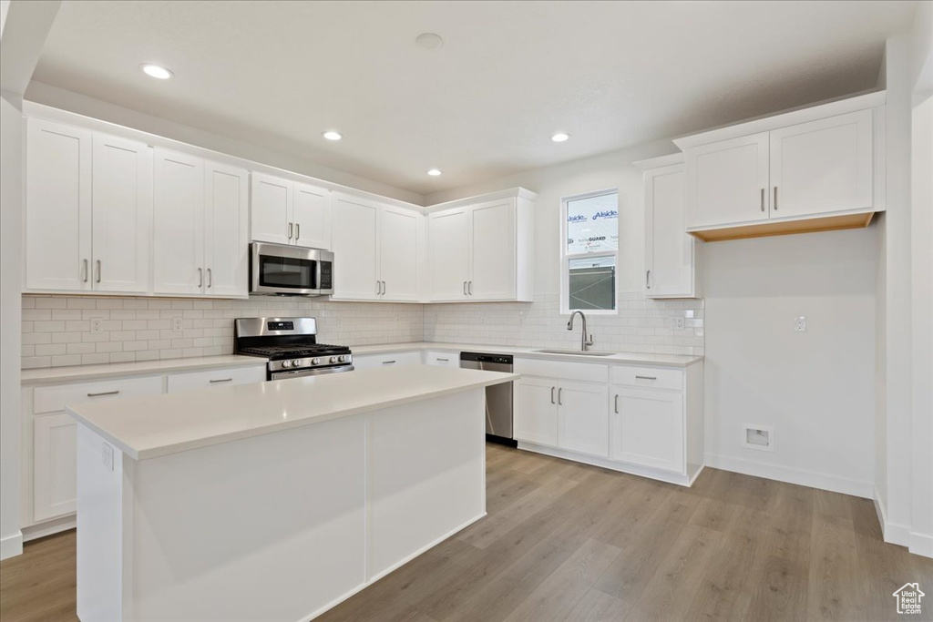 Kitchen featuring a center island, white cabinetry, light wood-type flooring, appliances with stainless steel finishes, and sink