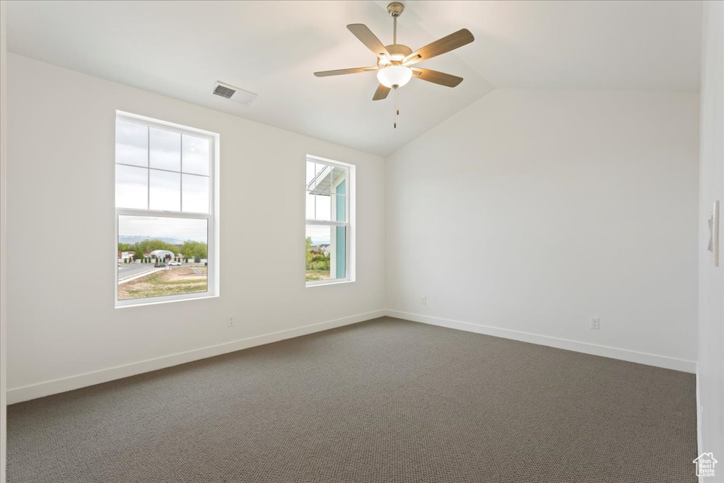 Empty room featuring plenty of natural light, dark colored carpet, and lofted ceiling