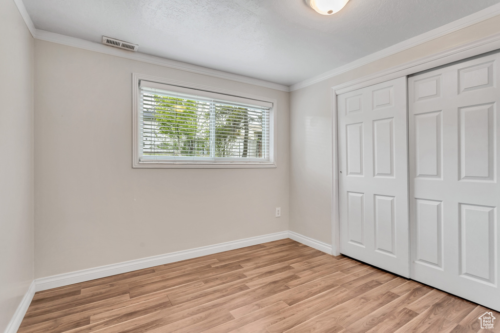 Unfurnished bedroom with crown molding, light hardwood / wood-style floors, and a closet