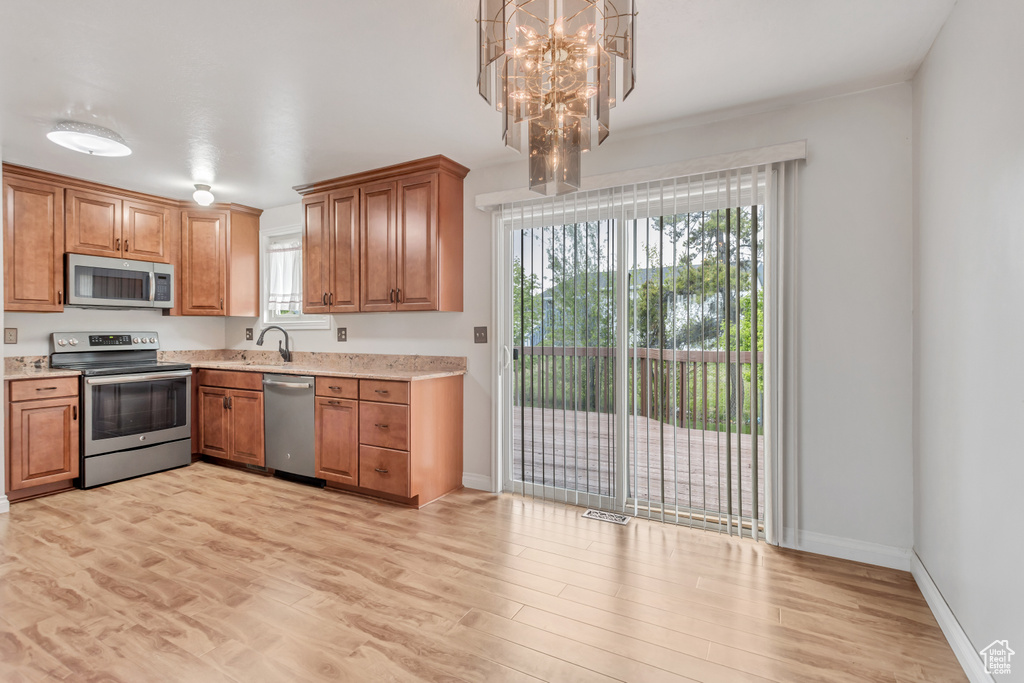 Kitchen featuring appliances with stainless steel finishes, a wealth of natural light, light hardwood / wood-style floors, and an inviting chandelier