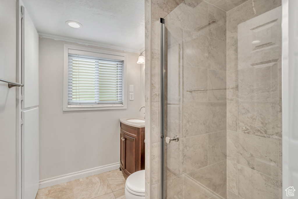 Bathroom featuring a shower with shower door, vanity, crown molding, and tile floors