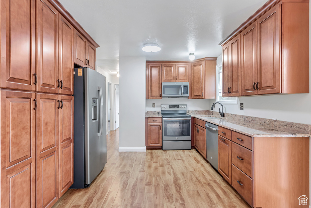 Kitchen featuring appliances with stainless steel finishes, light hardwood / wood-style flooring, sink, and light stone countertops