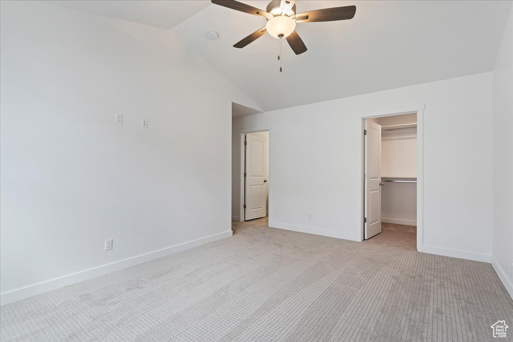Unfurnished bedroom with a closet, a spacious closet, vaulted ceiling, light colored carpet, and ceiling fan