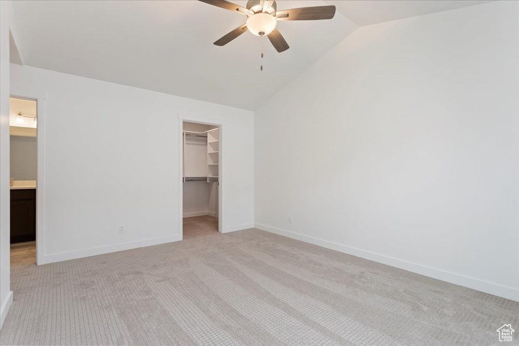 Unfurnished bedroom featuring a closet, ceiling fan, light colored carpet, lofted ceiling, and a spacious closet