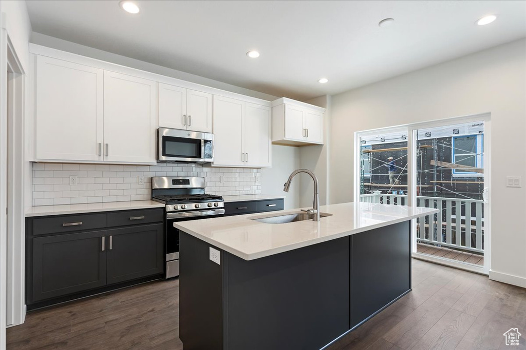 Kitchen featuring appliances with stainless steel finishes, dark hardwood / wood-style floors, tasteful backsplash, a kitchen island with sink, and sink