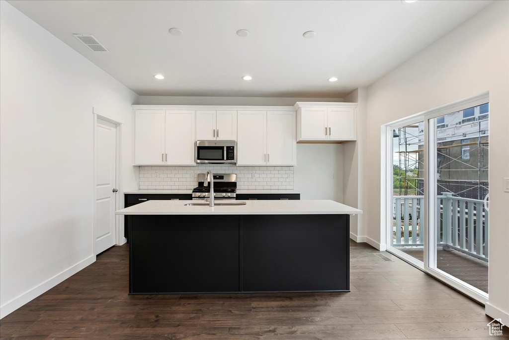 Kitchen with appliances with stainless steel finishes, dark hardwood / wood-style floors, white cabinetry, and a kitchen island with sink