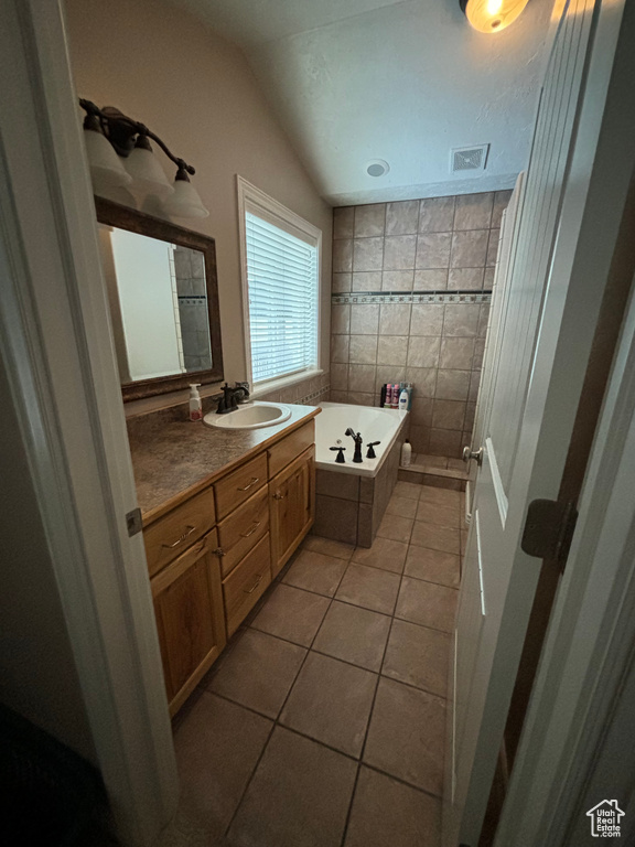 Bathroom featuring tile walls, vaulted ceiling, a washtub, tile flooring, and vanity