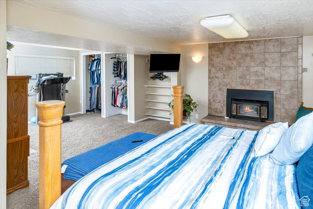 Carpeted bedroom with a closet, tile walls, a fireplace, a textured ceiling, and a walk in closet