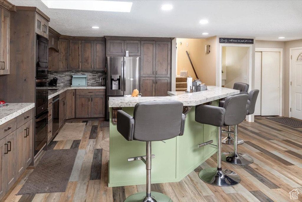 Kitchen with a kitchen island, hardwood / wood-style floors, tasteful backsplash, and light stone counters