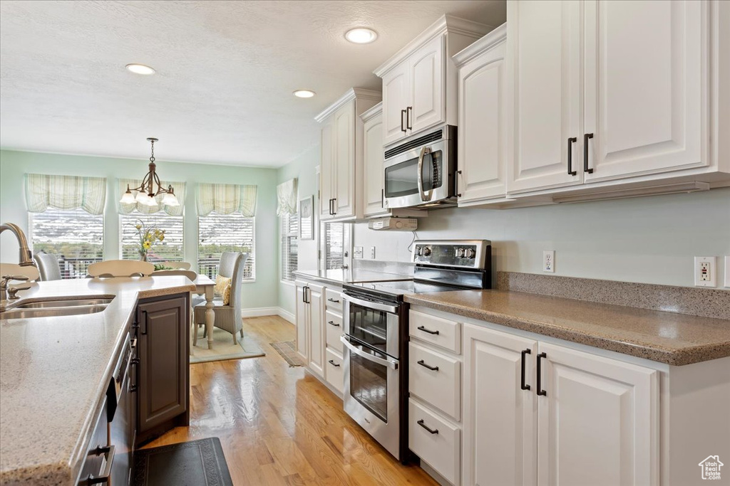 Kitchen with decorative light fixtures, appliances with stainless steel finishes, light hardwood / wood-style flooring, white cabinets, and sink