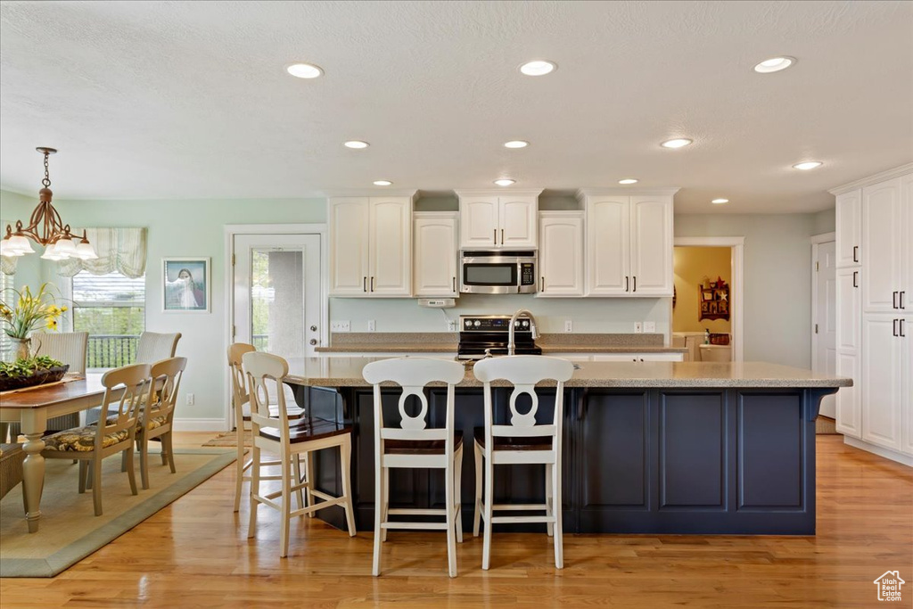 Kitchen with light wood-type flooring, an island with sink, white cabinetry, and pendant lighting