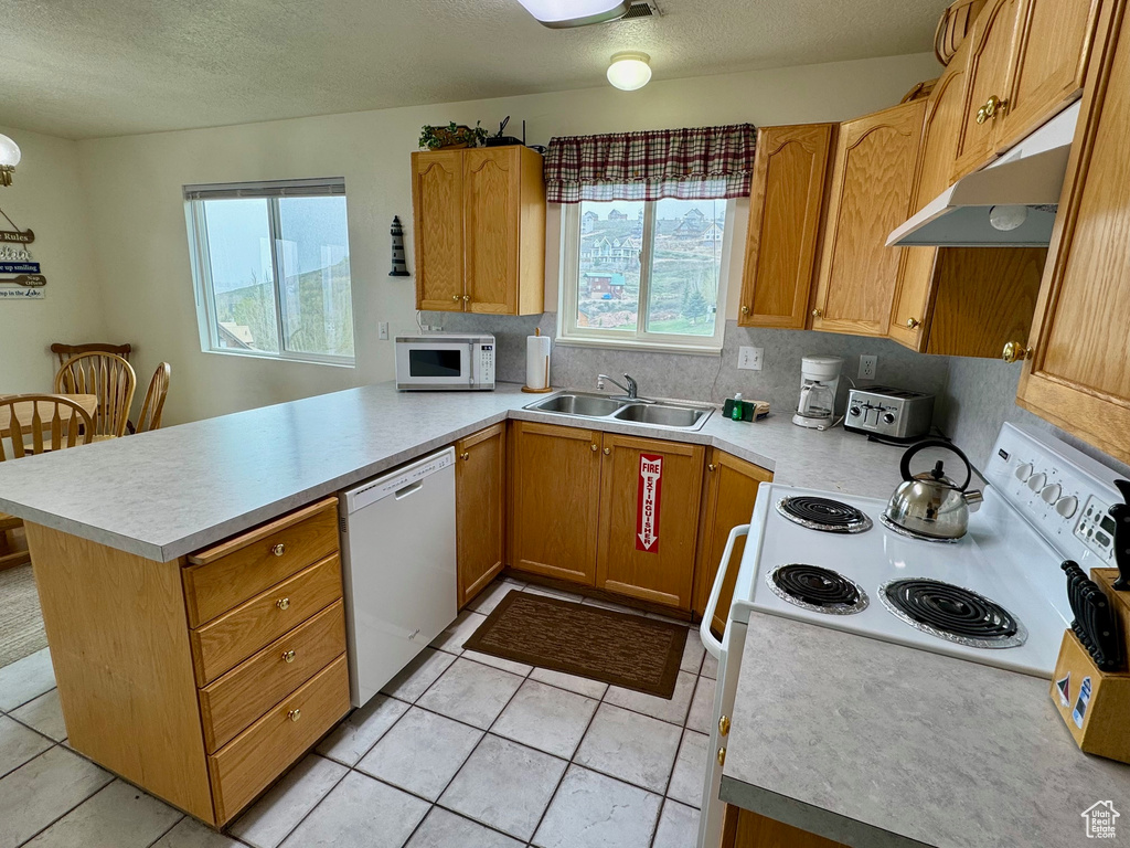 Kitchen with white appliances, backsplash, kitchen peninsula, light tile floors, and sink