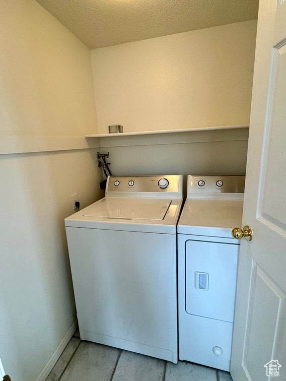 Laundry area featuring a textured ceiling, washing machine and dryer, and light tile floors