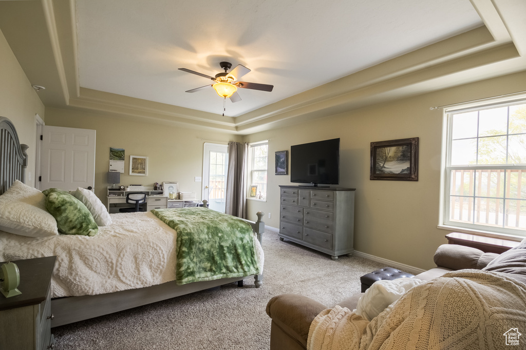 Bedroom featuring light colored carpet, ceiling fan, a tray ceiling, and multiple windows