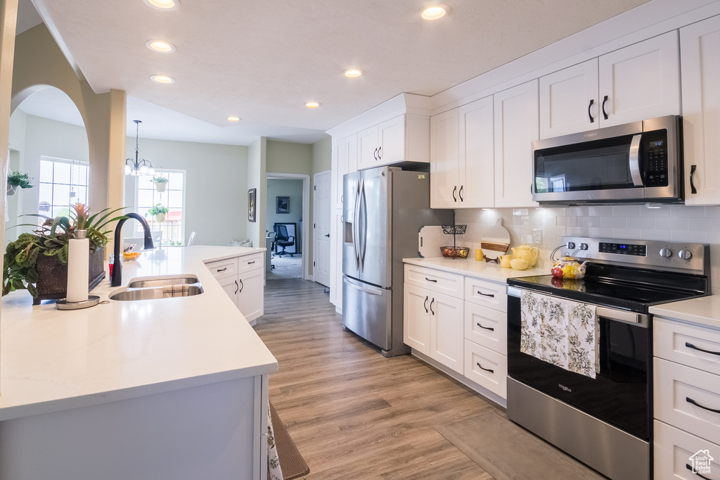 Kitchen featuring white cabinets, light wood-type flooring, backsplash, appliances with stainless steel finishes, and sink