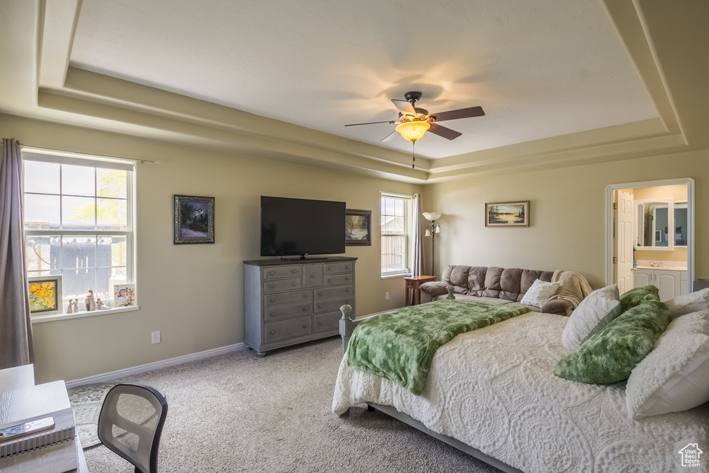 Carpeted bedroom with ceiling fan, a tray ceiling, and connected bathroom