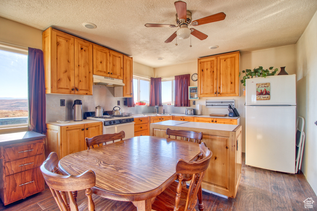 Kitchen featuring ceiling fan, a center island, a textured ceiling, white appliances, and dark wood-type flooring