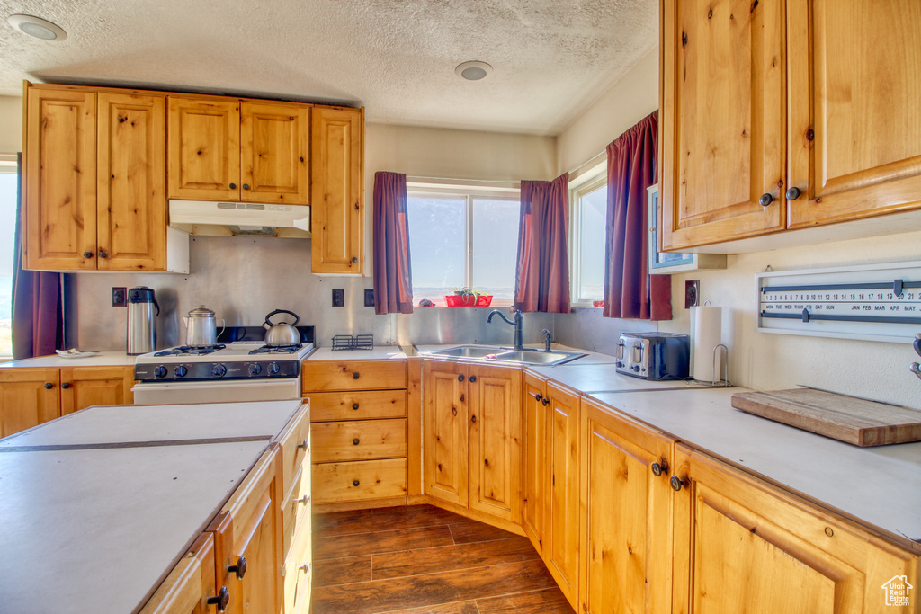 Kitchen with a textured ceiling, sink, white range with gas stovetop, and dark wood-type flooring