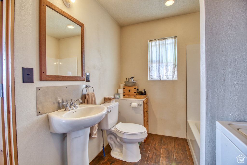 Bathroom with bathing tub / shower combination, hardwood / wood-style flooring, washer / dryer, toilet, and a textured ceiling