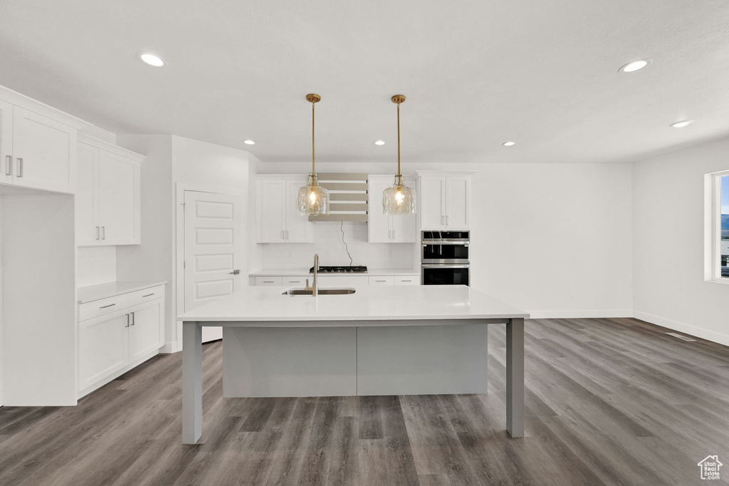 Kitchen with white cabinetry, a center island with sink, stainless steel double oven, and wood-type flooring